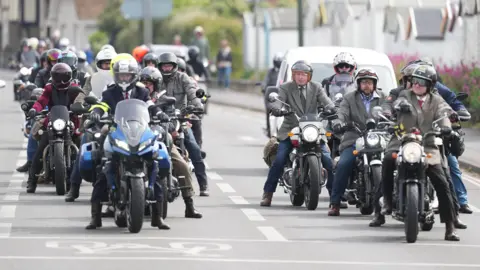 Eddie Mitchell A large group of motorcyclists wait at traffic lights.