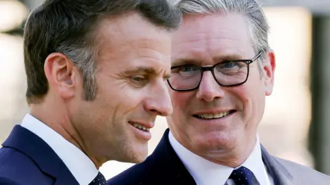 A close up of Starmer and Macron, whose heads are close together, with Starmer smiling at the French president