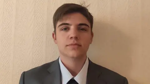 Yaroslav poses for the picture. he is in a shirt, tie and blazer. It is a close up of his head and shoulders. He has brown hair 