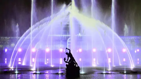 The Palm House at Kew Gardens is illuminated with a light show during a preview for the Christmas at Kew event on November 15, 2022 in London, with the Hercules statue in a silhouette in front of it. 