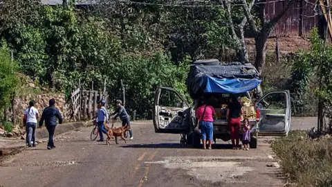 Getty Images Street in Concordia, Mexico. A car and several people are in the foreground, with houses and trees on a gill in the background