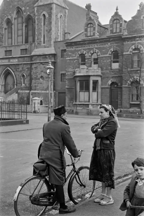 Bert Hardy/Getty Images A man and a woman in conversation on a street. The man is on a bike.