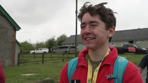 Alex smiling and looking to the left. He's wearing a red fleece and a blue rucksack. 