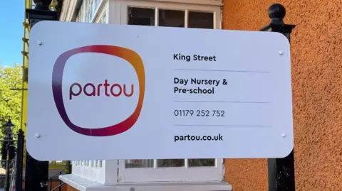 A sign outside the nursery, showing a logo, and the nursery's phone number and website