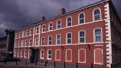 Havelock House, a red building with white outlines painted round the windows. There are cars parked at the front and a cloudy grey sky.