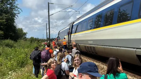Several passengers stood on leafy ground by the side of the train
