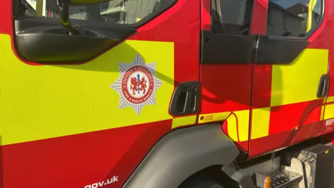 A red and yellow fire engine has the Devon and Somerset logo by its door.