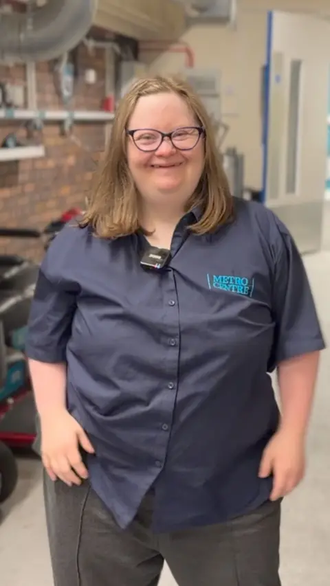 A smiling woman stands in a work uniform in a parking garage for wheelchairs.