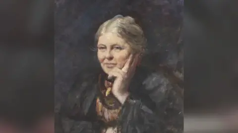 Portrait in oils dating from the turn of the 20th Century of an elderly woman. She appears to be seated and is holding her chin in her left hand. Her hair is grey and she is wearing a dark grey coat over a dress in muted shades of brown, orange and maroon.