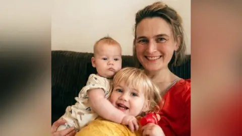 Family handout Kitty Hyde, who is wearing a top, is sitting on a couch and cuddling her two children. 