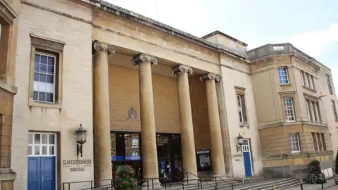 An exterior view of Gloucestershire County Council's headquarters. The building is built of light-coloured stone and has four large stone pillars supporting the front porch. 