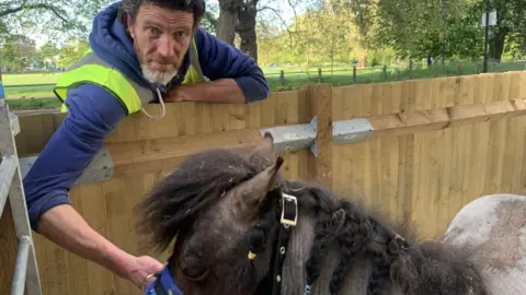 A middle-aged man with a horse, the horse has braided hair. The man has thick black hair and a great beard