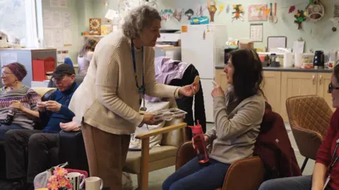 Open House Pictures / UoS A shot from the film, showing older people sat around a room listening to music, whilst eating biscuits.