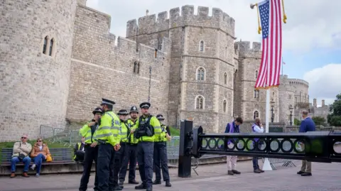 Getty Images A group of police officers in high-viz jackers huddle together outside Windsor Castle. Members of the public can be seen dotted around, including some sat on a bench behind where the officers are stood.