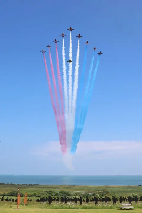 Chris Jackson/Getty Images The Red Arrows with a Eurofighter EF-200 Typhoon accompanying them flypast the UK Ministry of Defence and the Royal British Legion’s commemorative event at the British Normandy Memorial to mark the 80th anniversary of D-Day on June 06, 2024 in Ver-Sur-Mer, France. 