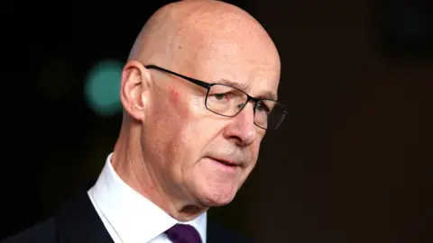 PA Media A close-up image of John Swinney, a bald man with glasses with a dark suit and white shirt