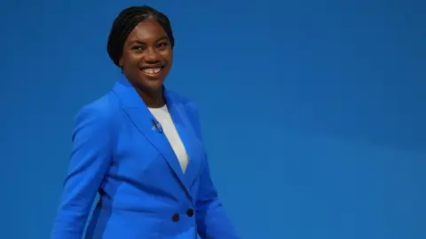 PA Media Kemi Badenoch smiles as she walks on stage wearing a blue blazer to deliver a speech during the Conservative Party Conference in October