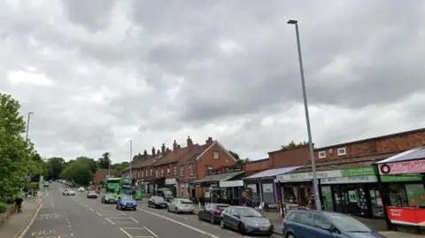 A main road with a parade of shops and cars parked on the roadside.
