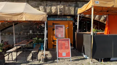 An exterior view of the Dorothy Pax at Victoria Quays, with tables and seats underneath gazebos.