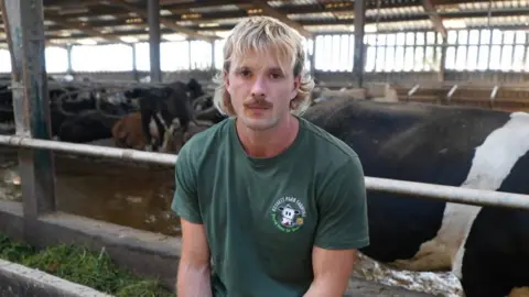 Un hombre con cabello rubio largo y bigote que lleva una camiseta verde.