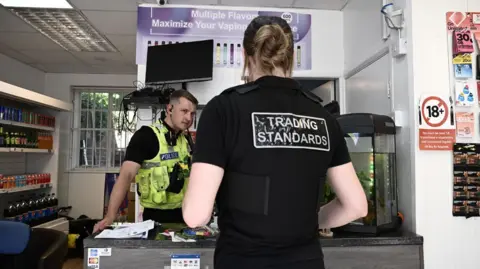 Lincolnshire County Council A male police officer standing at a vape shop counter with the back of a female Trading Standards officer in front of the desk