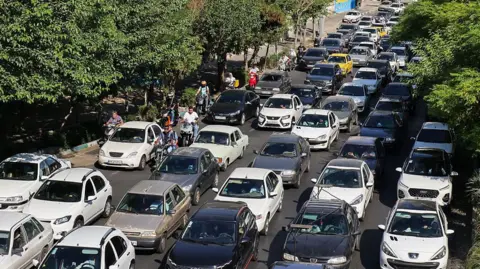 Vehicles wait in lines of traffic as people queue to get out of Tehran through road in the west of the city on 15 June 2025