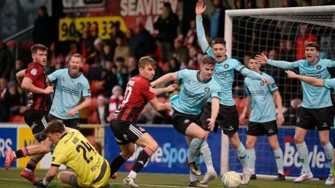 Pacemaker Action from the north Belfast derby at Crusaders' ground, Seaview. A number of players on the green pitch are featured from both Crusaders, in red and black, and Cliftonville in light blue and black.