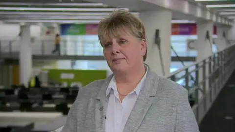 Lezley Picton standing on a balcony at BBC Birmingham's Mailbox studios, being interviewed while wearing a grey blazer and white shirt.