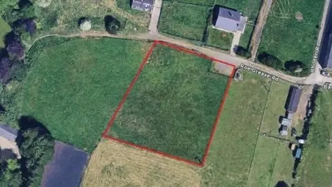 Ariel view of a plot of land off Roe Greave Road in Oswaldtwistle, showing patchwork fields and trees and three clusters of buildings.