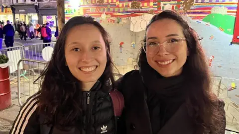 Maria Fernanda Kobayashi (left) and Ana Olivia Laurentino (right) both smiling at the camera with dark hair and dark clothing