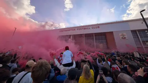 fans gathered out the front of St Mary's stadium with red flares smoking.