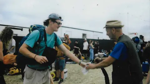 WaterAid A film photo showing a WaterAid volunteer refilling a man's water bottle using a small hose.