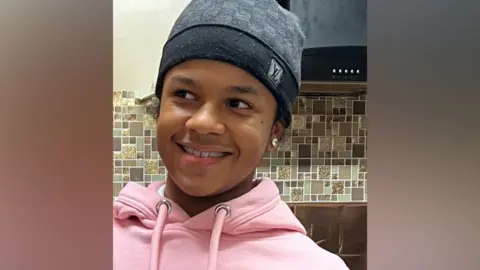 PA Media Leonardo Reid in a pink hoodie and grey beanie hat. He smiles and looks to one side.