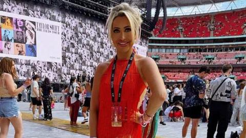 Image of Holly wearing an orange fringed leotard with a big screen and crowds behind her at Wembley