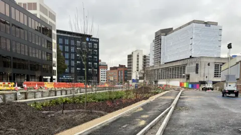 New roads bisected with a long strip of freshly planted trees and shrubs with the Zurich and Debenhams buildings in the background