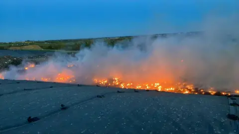 Cambridgeshire Fire and Rescue Service A drone image of a large fire at a landfill site. A large stretch of land is on fire and there is a large plume of smoke.