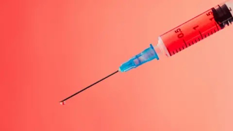 Stock image of needle with red liquid in it. The background of the needle is red tinted. 