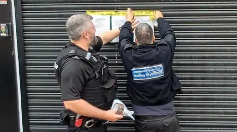 Members of Nottingham Trading Standards and Nottinghamshire Police place closure orders on a black shuttered shop