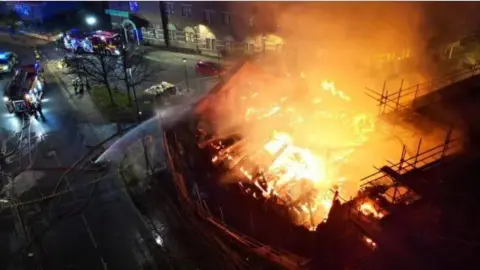 Michael Wilkinson An aerial view of the Wesley chapel on fire. Flames are engulfing the roof of the structure. A large stream of water is coming from a fire engine to extinguish the blaze.