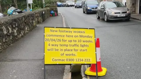 A temporary yellow road sign in Newlyn is in the road informing motorists that 4 way traffic lights will be in place for 10 weeks 