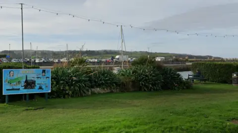 Generic Google image of Hayle in Cornwall. A blue sign, which reads Hayle, is on a grass area. 