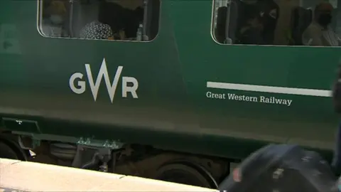 Green train carriage that has silver letters GWR which stands for Great Western Railway.