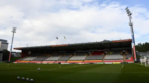 SNS Empty Firrhill Stadium stand with floodlights at the side and balls on the pitch 