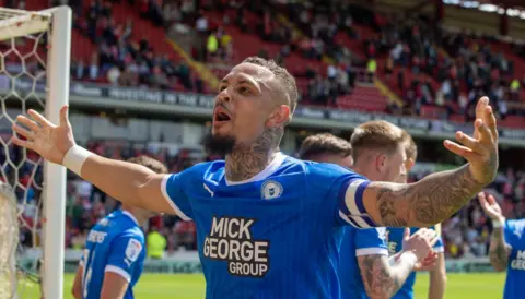 PA Media Peterborough United's Jonson Clarke-Harris celebrates after scoring a goal, with his arms outstretched.