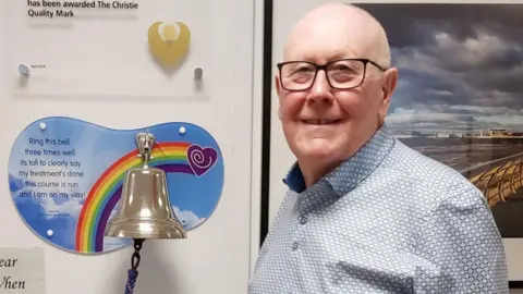PA Tom Critchley poses by a bell to celebrate all-clear