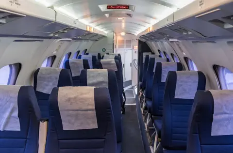 Highland Council Blue chairs inside a white aircraft cabin which is lit with bright lighting on the ceiling 