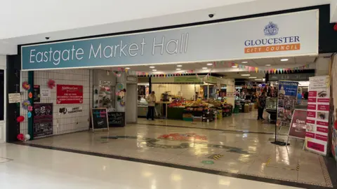The entrance to Eastgate Market Hall - a dated indoor market at a shopping centre, where trader stalls can be seen inside.