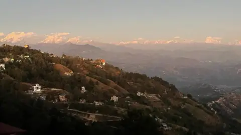 Yogendra Shakya View of a hill in the foreground with Himalaya mountains and some peaks visible in the background