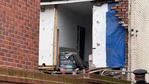 close-up image of upstairs bedroom at rear of house with bricks blown off, exposing back bedroom