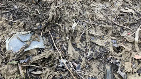 A close up image of sludgy brown wet wipes congealed together with mud and other litter from the river.